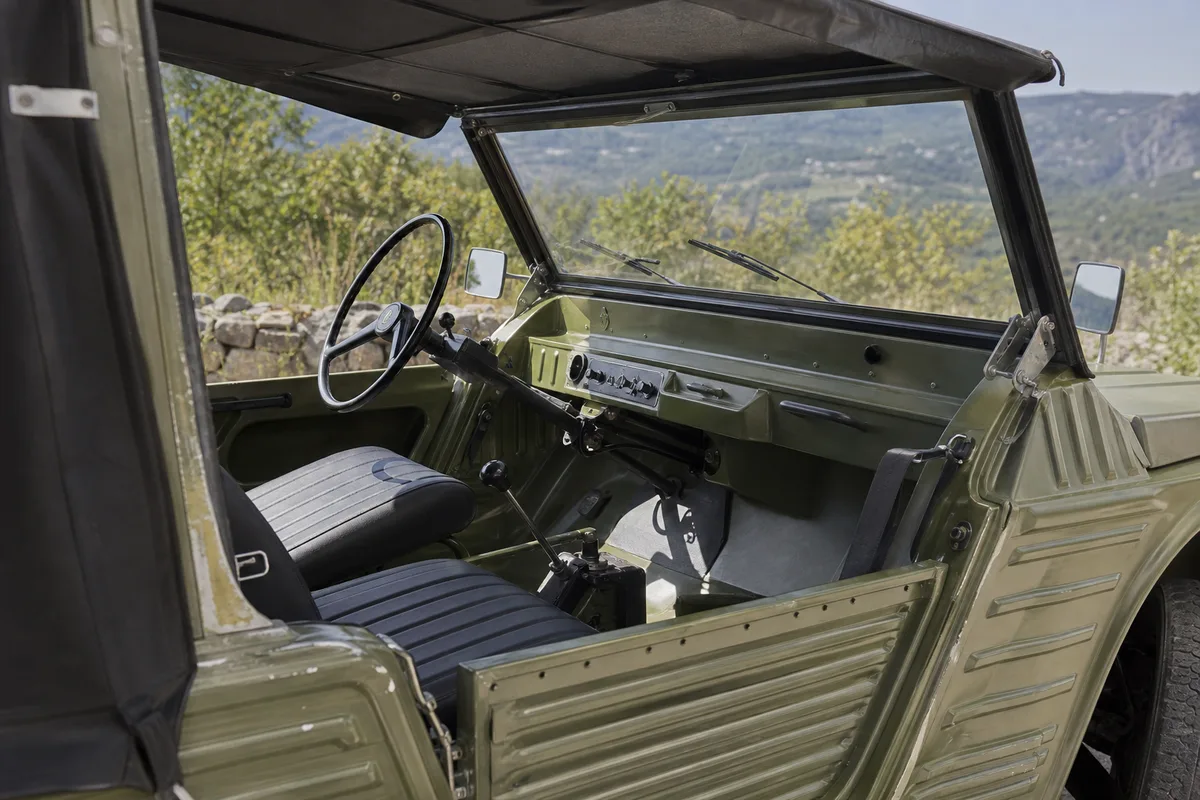 Habitacle dépouillé d’une Citroën Méhari avec sièges simples et volant fin, capote ouverte