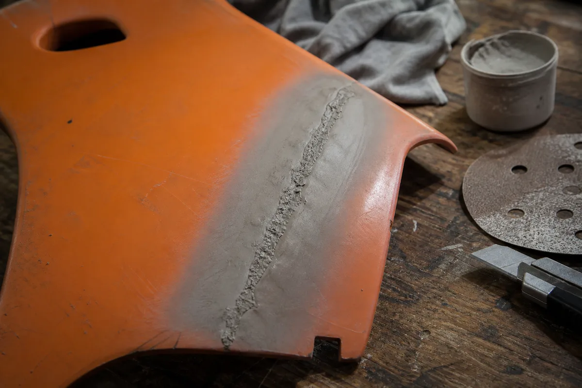 Détail d&rsquo;un panneau plastique orange en cours de réparation, fissure comblée et surface poncée